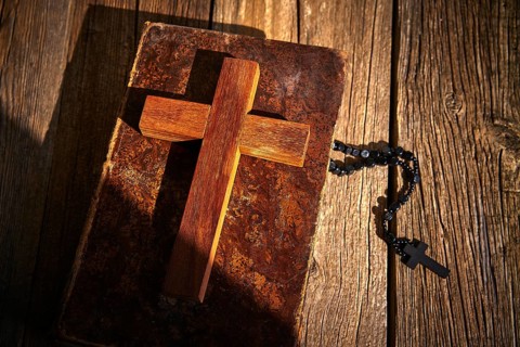 Christian cross on wood bible and rosary beads over wooden vintage background