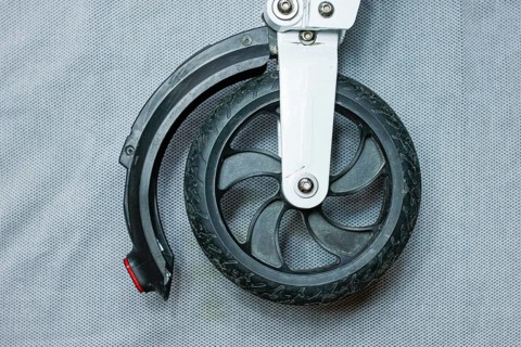 Front wheel and tire of a scooter with a black tire and metal attachment on a grey backdrop