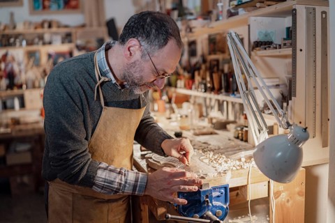 A craftsman meticulously shaping a violin part, surrounded by woodworking tools