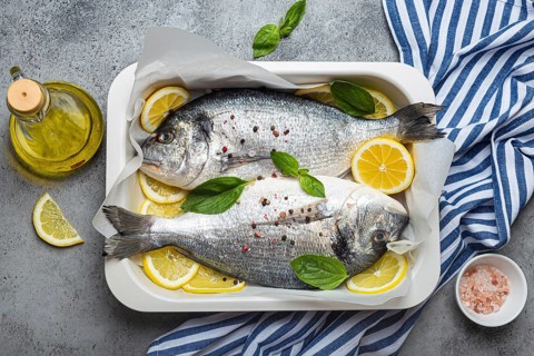 Raw fish dorado in casserole dish with ingredients lemon, fresh basil, bottle of olive oil on
