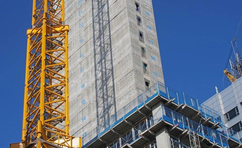 Close up of a large urban construction site with a yellow tower crane casting a shadow on a large