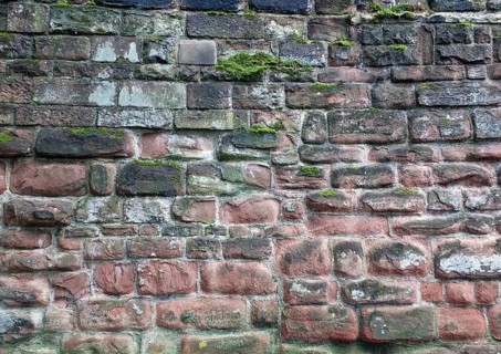 Full frame image of an ancient sandstone wall in red and black colors with sodd and algae growing