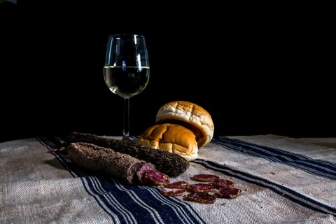 Still life table with a glass of white wine assorted dry sausages and bread on a flour cloth with