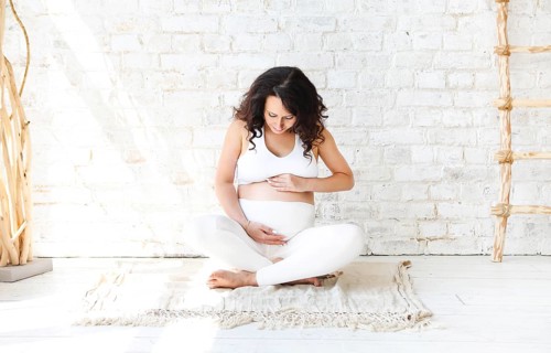 Beautiful brunette pregnant woman stretching and practicing yoga at home