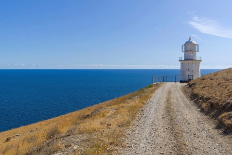 A dirt road running along a deserted mountainside to a lighthouse on the seashore. Cape Meganom,
