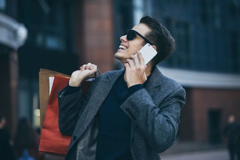 Positive cool guy with sunglasses and paper bags walking near showcase with reflection