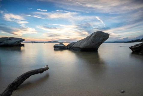 View through rocks on a sandy beach into the sunset. Landscape shot with view to the horizon over