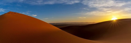 A panorama view of the sand dunes at Erg Chebbi in Morocco at sunset with a sunstar