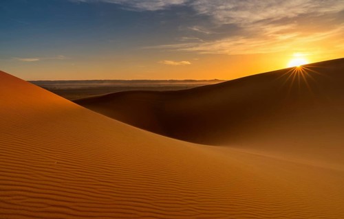 A view of the sand dunes at Erg Chebbi in Morocco at sunset with a sunstar