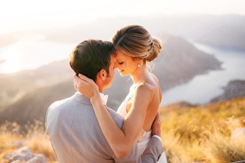 The bride and groom sitting on the top of Mount Lovcen overlooking the Bay of Kotor, smiling and