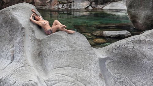 A woman lying in a comfortable position on a smooth granite rock on the bank of a river, Verzasca