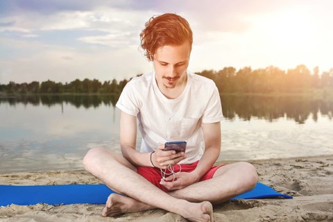 Man is sitting on the beach at lake and writing a sms on phone. good mood. beautiful view