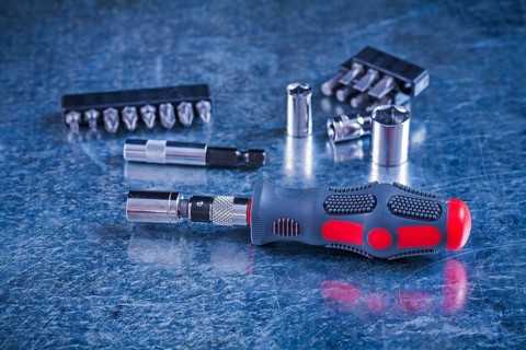 Insulated screwdriver with interchangeable bits and heads on scratched metallic background