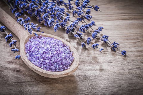 Dried scented curative lavender sea salt wooden spoon on wood board spa treatment concept