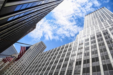 Low angle view of American flag and skyscrapers against sky in New York City. Finance, business and