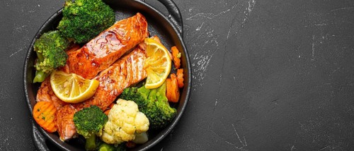 Healthy baked fish salmon steaks, broccoli, cauliflower, carrot in cast iron casserole bowl black