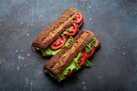 Two dark ciabatta sandwiches with green salad, ripe red tomatoes, onion and tuna on rustic concrete