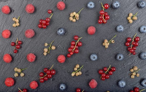 Flat lay view at ripe bilberry raspberry white and red currant on slate stone tray closeup