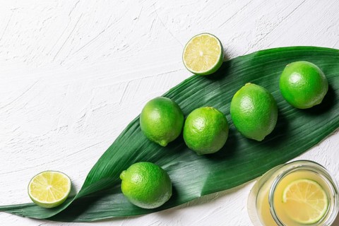 Bunch of limes on a big green leaf and a jar with freshly squeezed lime juice, on a white
