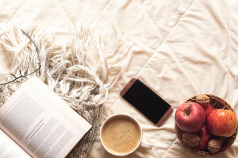 Coziness concept with an open book on a wool shawl, a basket with apples and nuts, a phone and a