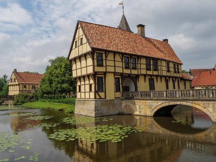 Half-timbered house stands picturesquely on a watercourse with water lilies and a stone bridge,