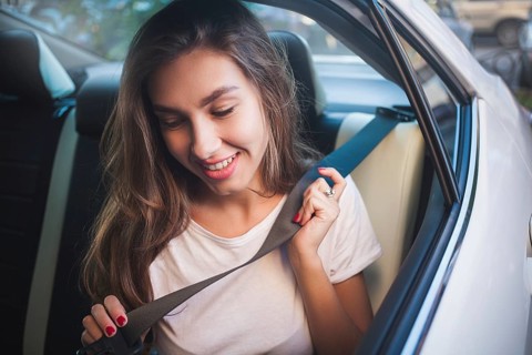 Beautiful woman with phone smiling while sitting on the back seat in the car