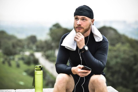 Muscular bearded athlete with towel checking burned calories on smartphone after good workout
