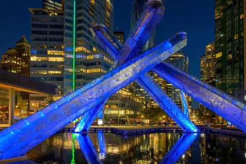 Modern Olympic fire installation at night with blue lighting and surrounding skyscrapers in the