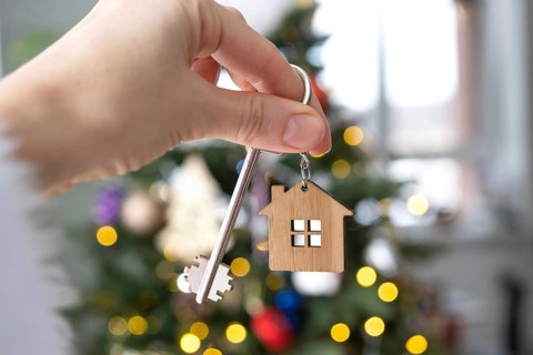 Key and tiny house keychain in hand on background fairy lights Christmas tree. gift for New Year,