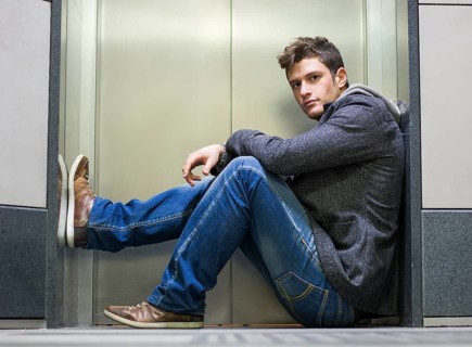 Handsome young man sitting in front of elevator (lift) doors, looking at camera
