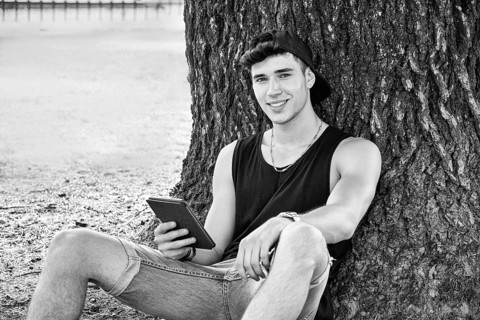 Smiling Young Handsome Man, Reading on Ebook Reader or Holding a Tablet Computer, Relaxing on