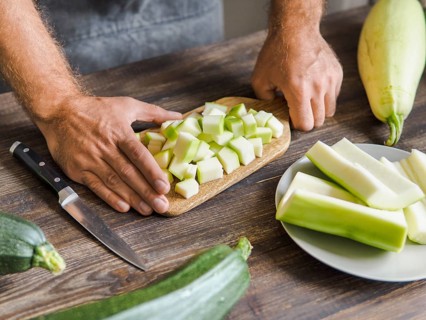 Zucchini harvest. Man slices zucchini cubes for freezing on wooden table. Farm organic zucchini