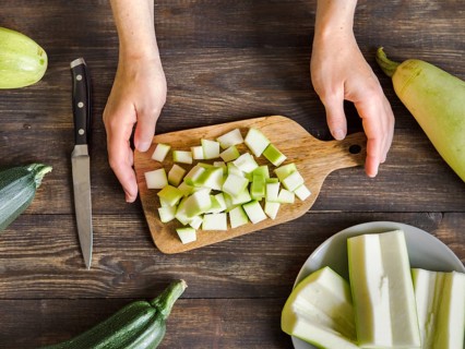 Zucchini harvest. Woman slices zucchini cubes for freezing on wooden table. Farm organic zucchini