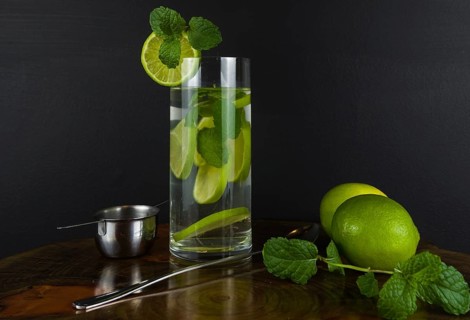 Glass of Mojito cocktail with mint and lime on a black board with fresh limes. Sparkling refreshing