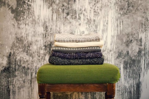 Pile of knitted warm grey and white blankets, scarves and woolen sweaters for winter or fall cold