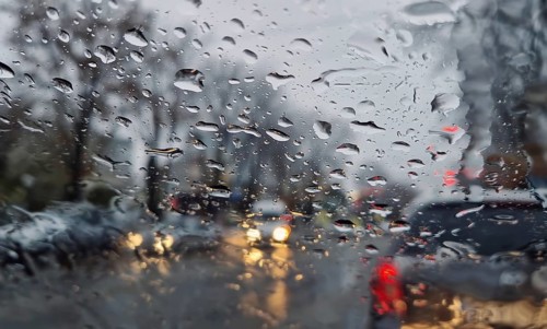 Melted snow and rain drops on the windshield of a car. Blurred outdoor view, winter season sleet as