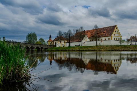 Old building and bridge reflected in a river under a cloudy sky, Tirschenreuth, Upper Palatinate,