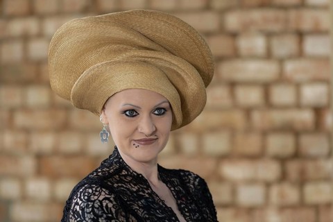 Woman in black lace dress with golden turban in front of beige wall, staged portrait shooting,