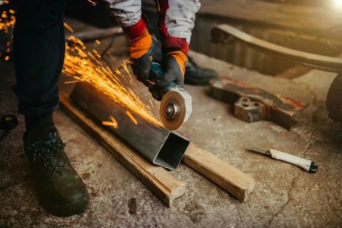 A worker grinding metal with sparks flying, wearing protective gloves