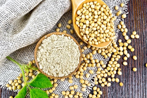 Soy flour in the bowl, soybeans in a spoon and on sackcloth, green soya leaf on a wooden board