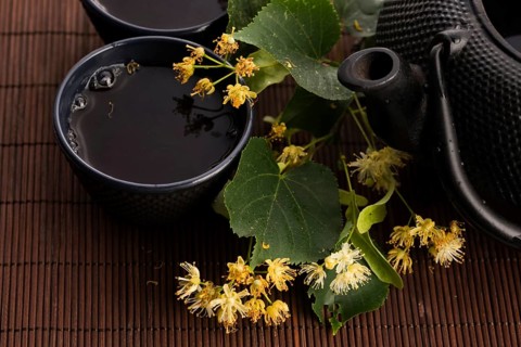Teapot and cup with linden tea and flowers