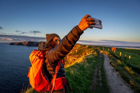 Female hiker taking a selfie, Cliffs of Moher, The Burren, County Clare, Ireland, United Kingdom,
