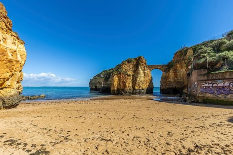 Yellow rocks and cliffs on a sandy beach. A bay by the sea, over which the old stone bridge of the
