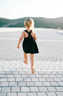 Little girl runs barefoot on a tiled road while hovering in the air. Back view.