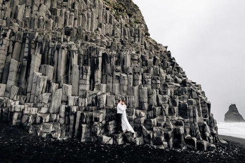 A wedding couple stands on a wall of stone pillars. The bride and groom are hugging on basalt
