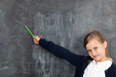 Schoolgirl shows on an empty school board. He is standing in the classroom at the chalkboard.
