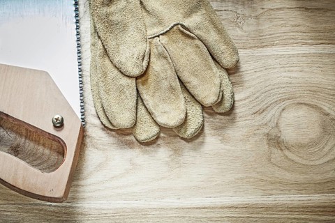 Safety gloves handsaw on wooden board top view construction concept