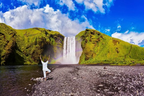 Elderly woman performs asana tree of hatha yoga before falling water. Grand waterfall with rainbow