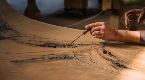 Hands adding resin to wood, focusing on intricate detailing and texture in a workshop setting