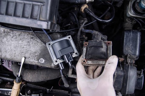 Close-up of a hand holding a car ignition coil in an engine